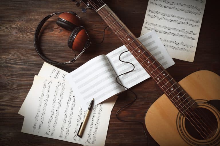 Music sheet, headset, a guitar and a pen on a table