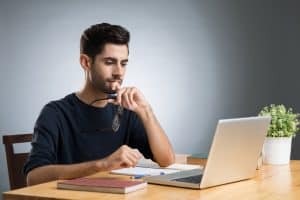 A male student looking at his laptop and pondering