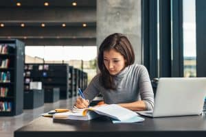 A woman in the library writing on her notebook