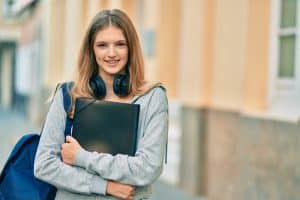 Female college student wearing headphones and carrying a binder.