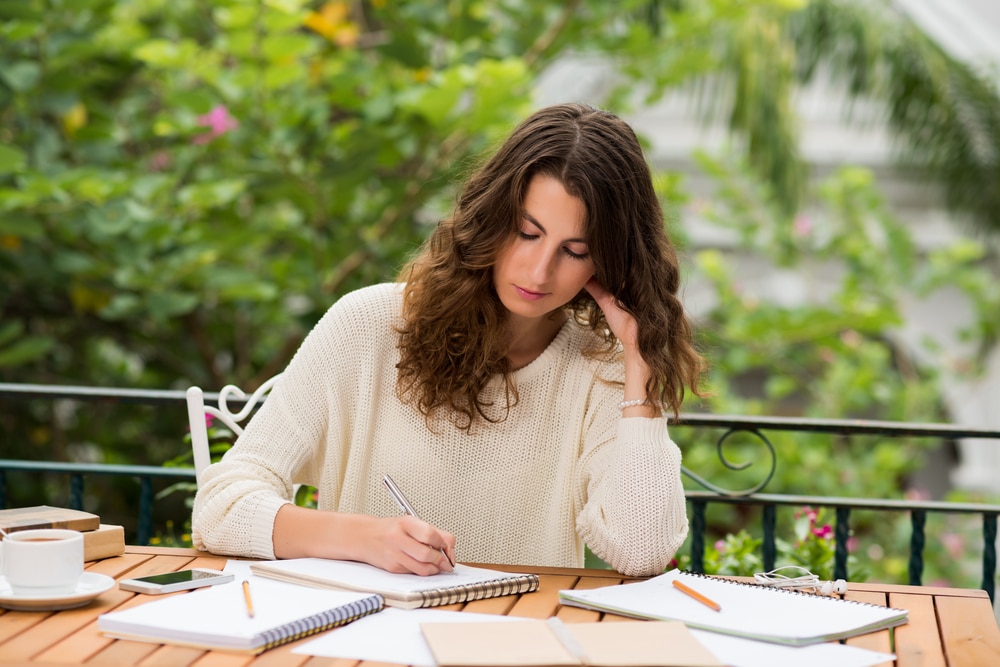 A woman with several notebooks in front of her is writing.