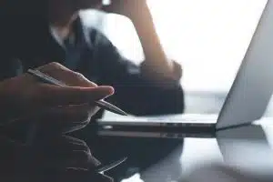 A person holding a pen with a laptop in front.