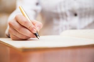 A person holding a pen, starting to write on a paper.