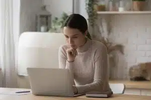 A woman with hand under her chin while looking at her laptop.