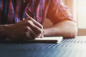 A male hand writing in a notebook using pen.