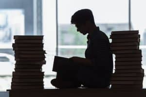 A silhouette of man reading a book while being surrounded by lots of books.