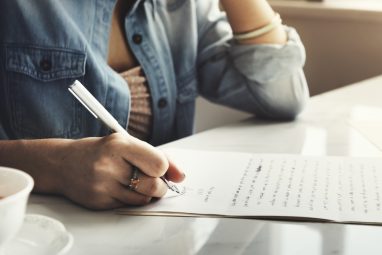 A female student writing an editorial by hand on paper, representing the thoughtful and persuasive writing style developed for the New York Times Student Editorial Contest.