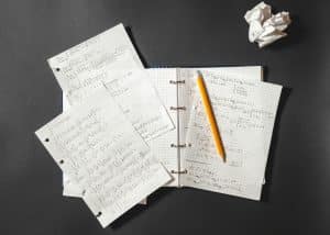 Mathematical problems in a notebook and crumpled piece of paper on a desk.