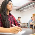 A female student listening to the class lecture while holding a pen.