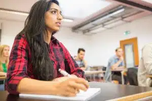 A female student listening to the class lecture while holding a pen.