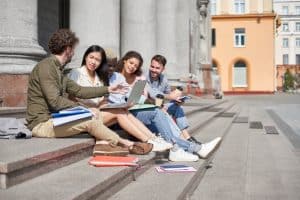 Group of students with a laptop are chatting while sitting on the stairs.