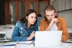 Two students sitting in classroom and studying together with laptop.