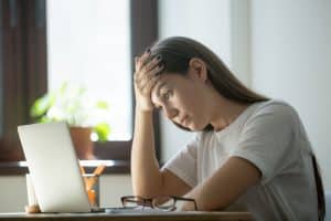 A woman looks at her laptop with a pained worried expression