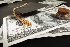 Mini graduation cap and coins on top of bills.