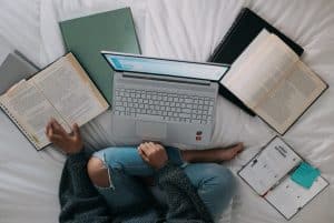 Students studying in a bed with notebooks and a laptop.