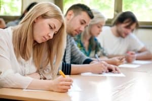 Young woman taking an exam with her fellow classmates.