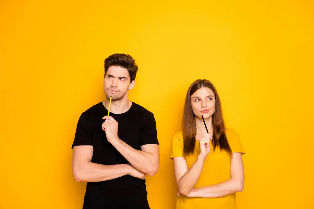 Two students thinking of something while leaning on a yellow wall.