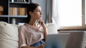 Young woman looking at the window with a laptop on her lap.