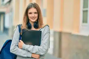 Female student clutching her book while smiling at the camera.