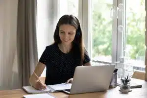 Female student writing while looking at his laptop.