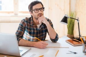 Young man looking away while in front of her laptop.