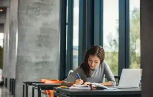 Female student studying near a window.