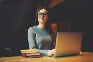 Young woman looking outside while typing in a desk with books.