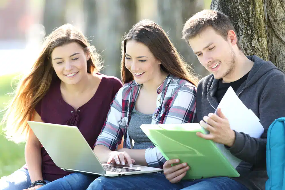Three students talking in a bench while holding their notes.
