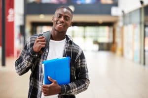 Young male student holding her book and backpack in a hallway.