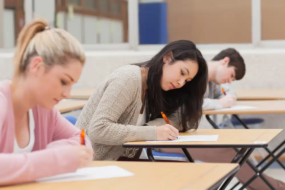 Students taking an exam on their desks in a classroom.