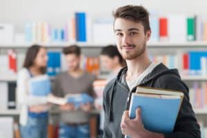 Male student holding books while smiling at the camera.