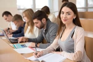 Female student smiling at the camera while her classmates are working on the table.