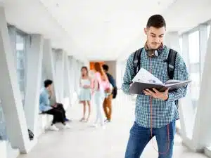 Male student reading a book in the hallway.