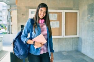 Female student holding her things while smiling at the camera.