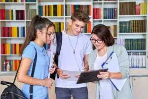 Two students talking to a teacher in a library.