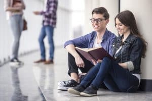 Two students talking while sitting on the floor.