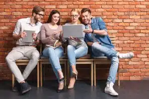 Students leaning on a wall while looking at a laptop.