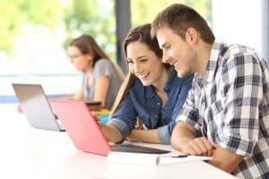 Two students talking in a desk with a laptop.