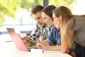 Three students using a laptop in a table.