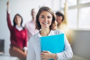 Female student holding a folder in a room with her classmates.