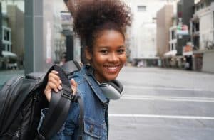 Young woman holding her bag while smiling at the camera.