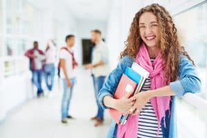 a student carrying her things and smiling in front of the camera