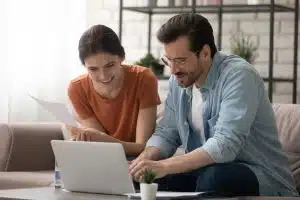 Two people talking in front of a laptop while sitting on the couch of a living room.