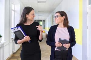 Two women are talking while walking in the hallway.