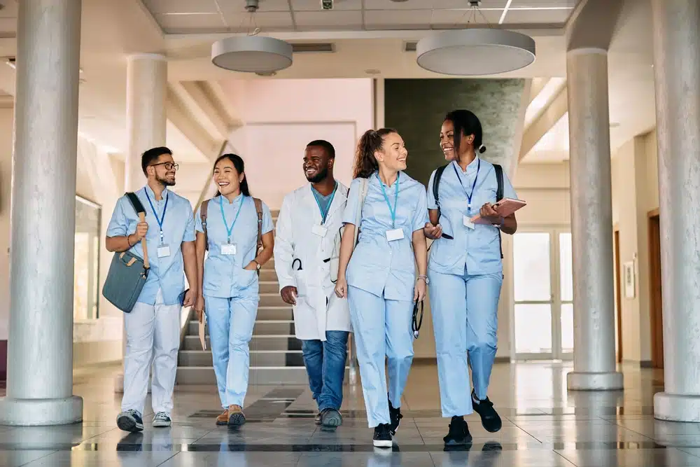 Five medical students wearing scrubs as they walk inside the lobby of a medical school
