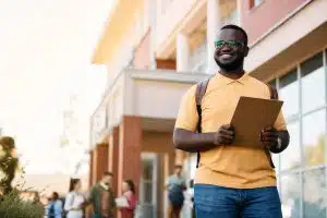 A male college student carrying a clip board and smiling widely