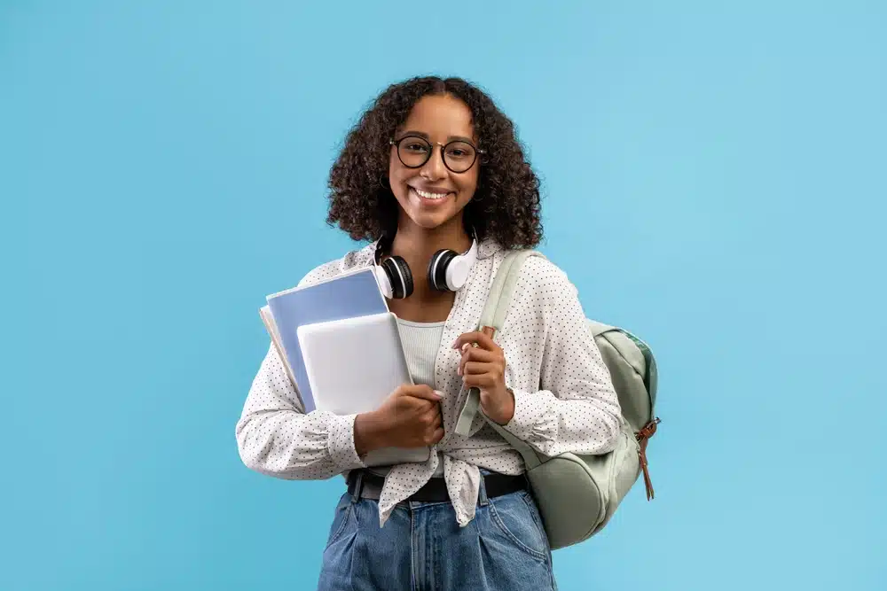a female student smiling in front of the camera and carrying her stuff