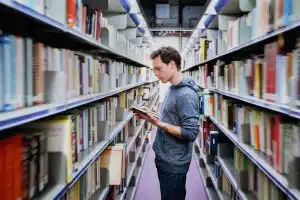 a male student reading a book in between shelves inside a library