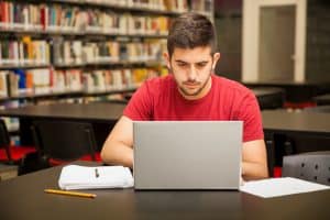 Male student typing in a table on a library.