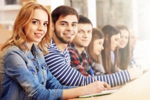 Grupo de estudantes sorrindo para a câmera sentada em uma mesa longa